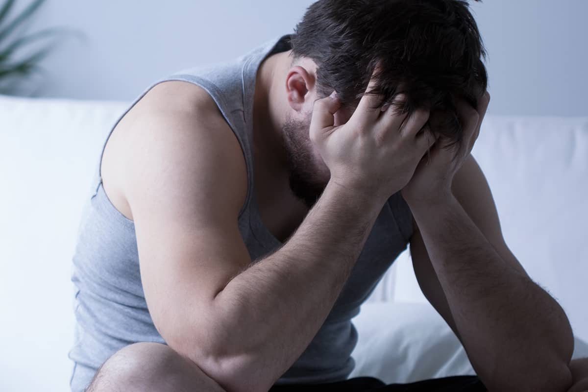 a man sits on his bed with his head in his hands as he thinks about depression and anxiety